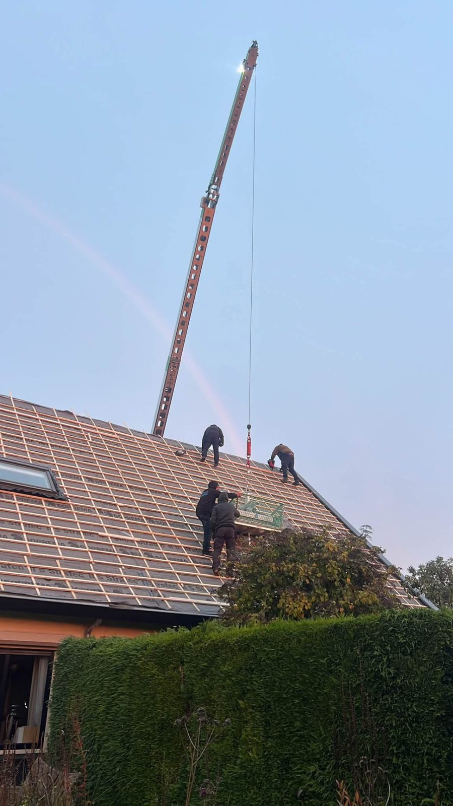 Dakdekkers van Dakspecialist Uner aan het werk op een hellend dak, met bouwkraan